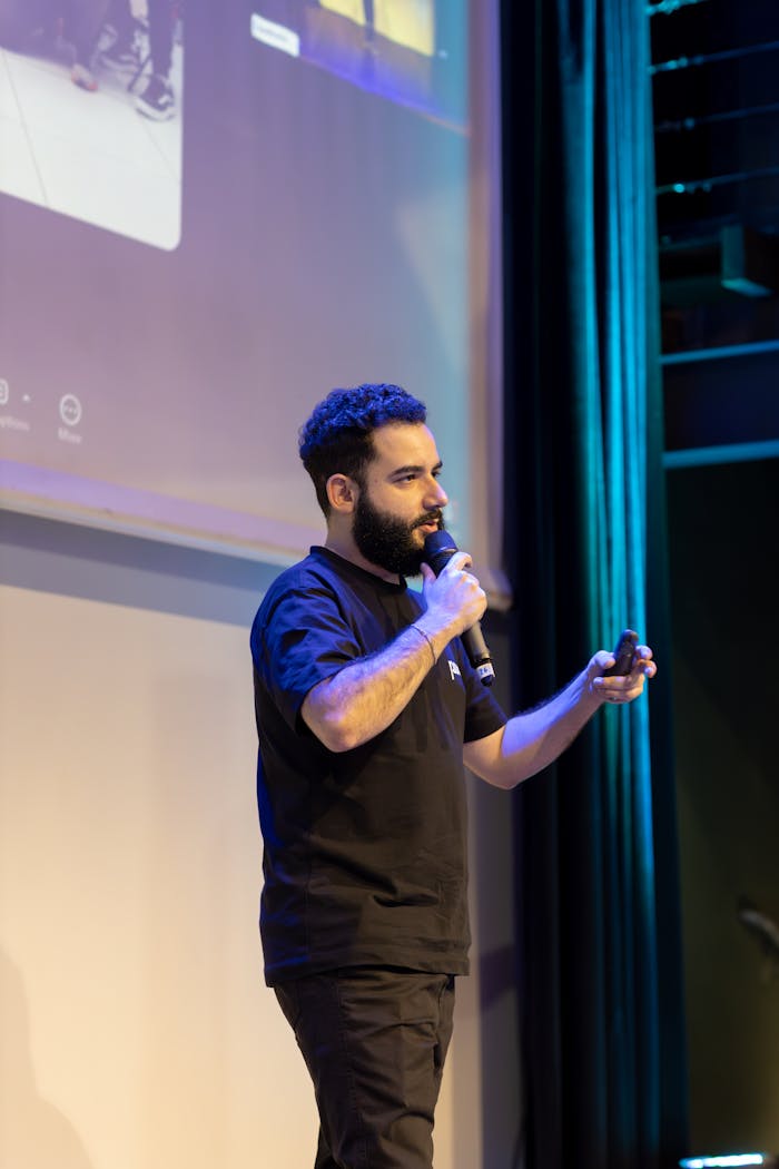 Services Man presenting on stage with microphone at a conference event.